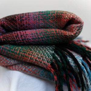 May include: A folded plaid throw blanket with fringe in shades of red, green, blue, and black.