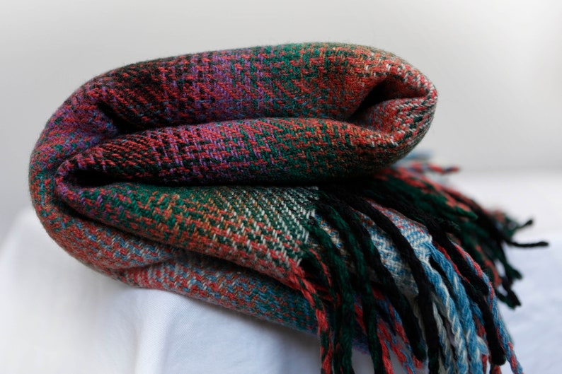 May include: A folded plaid throw blanket with fringe in shades of red, green, blue, and black.