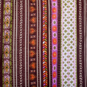 Puede incluir: Una tela marr&oacute;n con un patr&oacute;n repetitivo de rayas de colores y dise&ntilde;os geom&eacute;tricos. La tela presenta una variedad de colores, incluyendo naranja, rosa, verde y blanco.