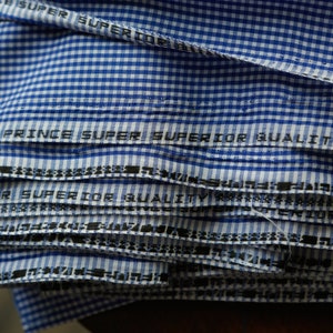 May include: Close-up of a stack of blue and white checkered fabric with the text "Prince Super Superior Quality" printed on the fabric.