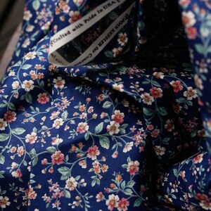 Pu&ograve; includere: Primo piano di un tessuto blu navy con un motivo floreale bianco e rosa. Il tessuto &egrave; piegato e ha un'etichetta bianca con il testo "Crafted with Pride in USA".
