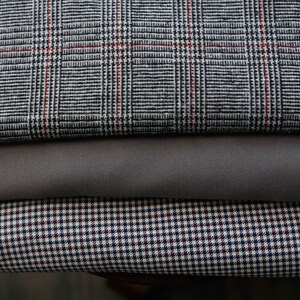 May include: Three different fabric swatches stacked on top of each other. The top swatch is a gray and white plaid with red accents. The middle swatch is a solid gray. The bottom swatch is a white and black gingham with red accents.