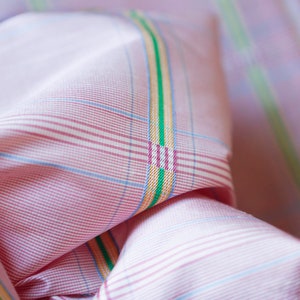 May include: Pink and white checkered fabric with thin green, yellow, and blue stripes. The fabric is folded and the stripes are visible on the fold.