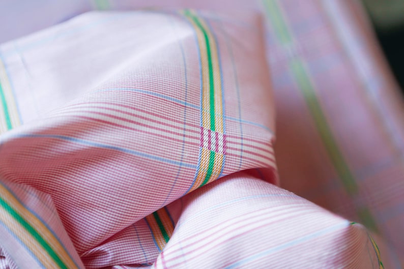 May include: Pink and white checkered fabric with thin green, yellow, and blue stripes. The fabric is folded and the stripes are visible on the fold.