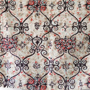 May include: A beige fabric with a repeating pattern of black, red, and blue swirls. The pattern is a traditional design with a geometric feel.