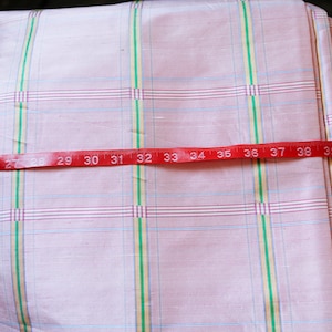 May include: Pink and white checkered fabric with a red measuring tape across it. The tape reads 24 to 40 inches.