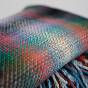May include: A colorful plaid throw blanket with fringe on the edges. The blanket is folded in half and the fringe is visible on the bottom edge.