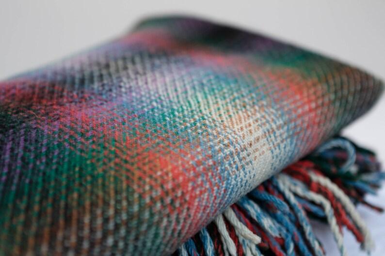 May include: A colorful plaid throw blanket with fringe on the edges. The blanket is folded in half and the fringe is visible on the bottom edge.
