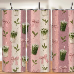May include: A cylindrical stainless steel tumbler with a lid and straw, featuring a repeating pattern of iced matcha lattes, pink bows, and green tea leaves on a textured background of vertical stripes in shades of light and dusty pink.