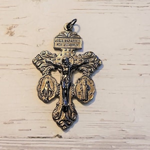 May include: A silver-toned crucifix pendant with intricate detailing. The cross features a figure of Jesus and includes two smaller medallions. The top of the cross has the inscription "JESUS NAZARENUS REX JUDAEORUM".