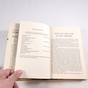 May include: An open book with a white cover and a yellow spine. The book is titled "Freezing and Canning Cookbook" and has a section titled "What You Will Find in This Cookbook". The text describes the book as a revised edition of the "Countryside Test Kitchen" cookbook from 1963.