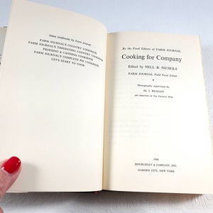 May include: Open book titled "Cooking for Company" by the Food Editors of Farm Journal. The book's pages are cream-colored with black text. The cover is partially visible, showing the title and author.