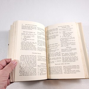 May include: An open vintage cookbook with pages showing recipes for fresh red raspberry jam, concord grape spread, and other fruit spreads. The book has a yellow cover with the title "Jams, Jellies and Other Spreads" printed in black.