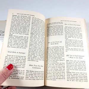 May include: Open vintage cookbook pages with text on how to make food taste wonderful. The pages are yellowed with age, and the book is held open by a hand with red nail polish. The book is titled "Cookery for the Food Connoisseur".