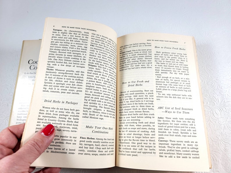 May include: Open vintage cookbook pages with text on how to make food taste wonderful. The pages are yellowed with age, and the book is held open by a hand with red nail polish. The book is titled "Cookery for the Food Connoisseur".