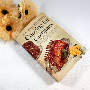 May include: A vintage cookbook titled "Cooking for Company" by the Food Editors of Farm Journal. The cover features images of cooked meat dishes on silver platters, with yellow flowers in the background.