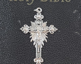 May include: A silver crucifix pendant with a detailed depiction of Jesus Christ on the cross. The cross is ornate with decorative flourishes and is set against a black background with the words "Holy Bible" in silver lettering.