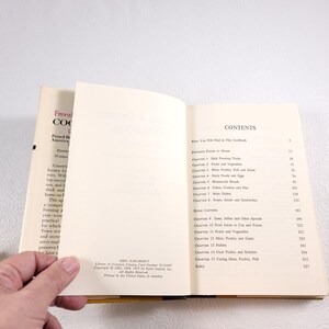 May include: A vintage cookbook titled "Freezing & Cooking" with a yellow spine and a white cover. The cover features the text "Prized Recipes from American Kitchens" and "Every Country Knows... What top success tries. Will you succeed?" The book has a contents page with chapter titles such as "Freezing Foods at Home", "Jams, Jellies and Other Spreads", and "Fruit Pickles and Relishes".