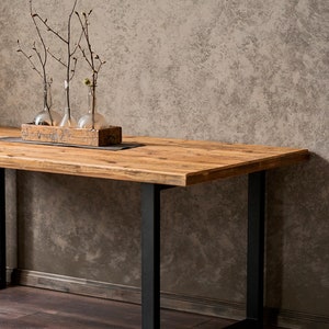 Dining table made of reclaimed pine boards and steel u-shaped legs. The durable metal legs are powder-coated black. The tabletop made from old boards has a pattern that reflects the antiquity and uniqueness of the product.