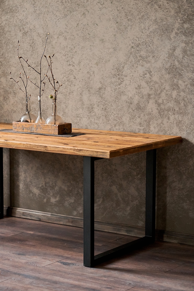 Dining table made of reclaimed pine boards and steel u-shaped legs. The durable metal legs are powder-coated black. The tabletop made from old boards has a pattern that reflects the antiquity and uniqueness of the product.