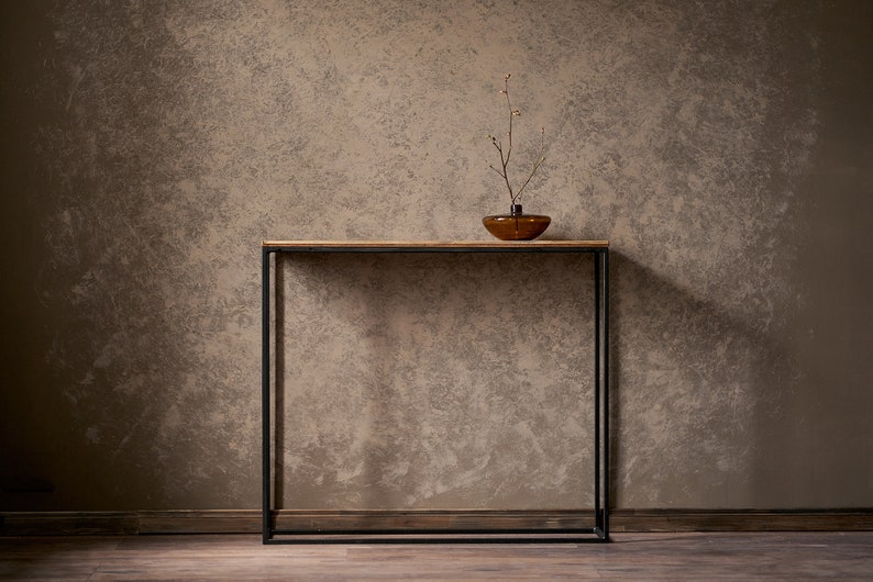 An elegant console made from old boards and a thin square pipe. A rectangular, powder-coated metal frame supports a wooden tabletop made from reclaimed planks.