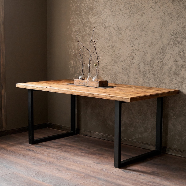 Dining table made of reclaimed pine boards and steel u-shaped legs. The durable metal legs are powder-coated black. The tabletop made from old boards has a pattern that reflects the antiquity and uniqueness of the product.