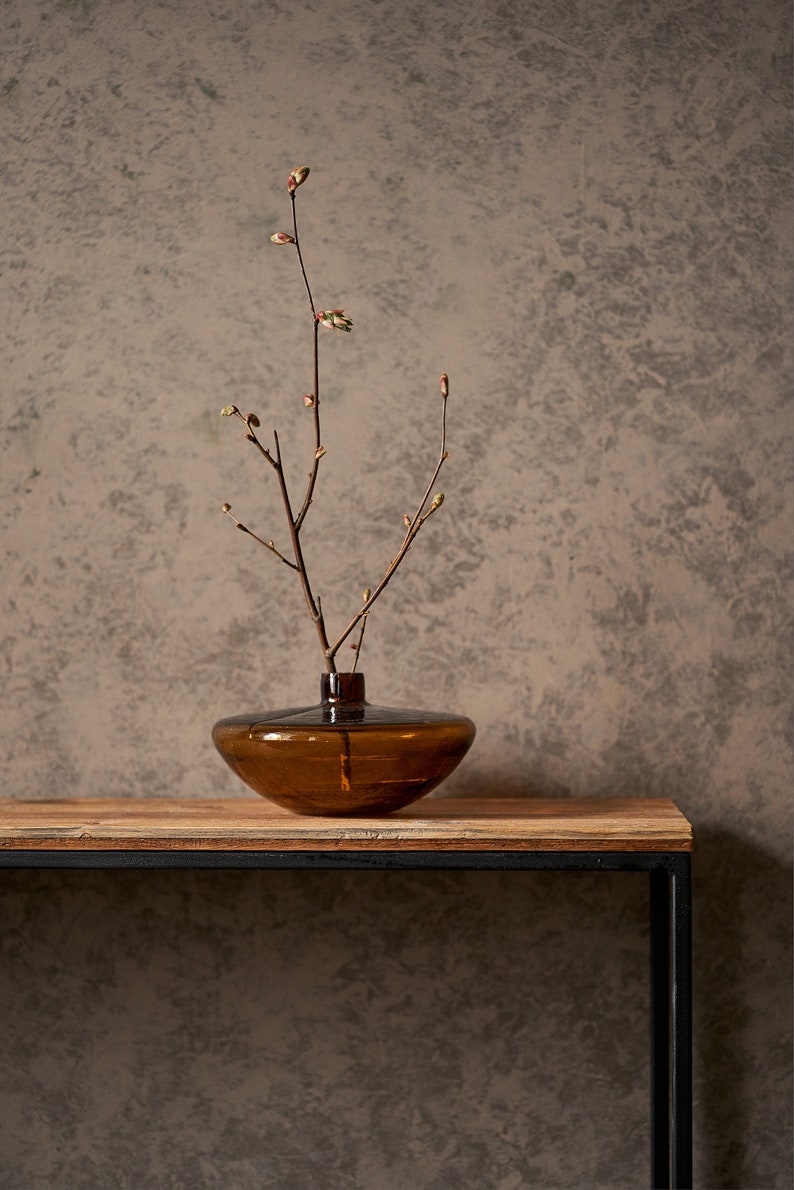 An elegant console made from old boards and a thin square pipe. A rectangular, powder-coated metal frame supports a wooden tabletop made from reclaimed planks. the thin tabletop has a unique pattern of old pine boards.