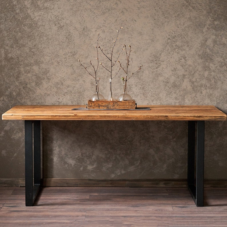 Dining table made of reclaimed pine boards and steel u-shaped legs. The durable metal legs are powder-coated black. The tabletop made from old boards has a pattern that reflects the antiquity and uniqueness of the product.