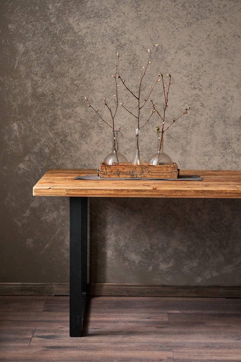 Dining table made of reclaimed pine boards and steel u-shaped legs. The durable metal legs are powder-coated black. The tabletop made from old boards has a pattern that reflects the antiquity and uniqueness of the product.