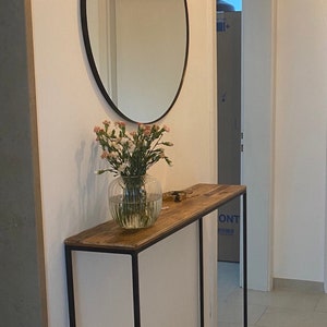 An elegant narrow and long console made from old boards and a thin square pipe. A rectangular, powder-coated metal frame supports a wooden tabletop made from reclaimed planks. the thin tabletop has a unique pattern of old pine boards.