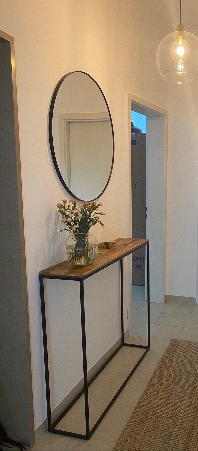 An elegant narrow and long console made from old boards and a thin square pipe. A rectangular, powder-coated metal frame supports a wooden tabletop made from reclaimed planks. the thin tabletop has a unique pattern of old pine boards.