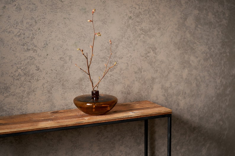 An elegant console made from old boards and a thin square pipe. A rectangular, powder-coated metal frame supports a wooden tabletop made from reclaimed planks. the thin tabletop has a unique pattern of old pine boards.