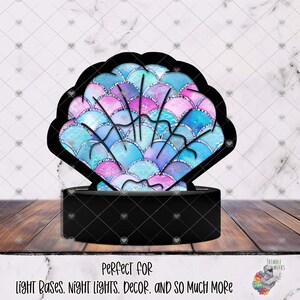 May include: A black seashell-shaped light base with a colorful, iridescent design. The shell features blue, pink, and purple scales with silver accents. The base has text that reads "Perfect for light bases, night lights, decor, and so much more."