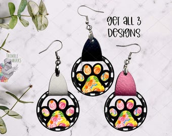 May include: Three pairs of dangle earrings featuring a circular black frame with a colorful paw print design in the center. Each earring has a textured leather-like top tab in silver, black, or pink. The text "GET ALL 3 DESIGNS" is visible.