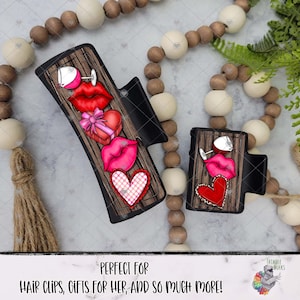 Puede incluir: Dos pinzas para el cabello negras con un diseño de vetas de madera. Cada pinza presenta una copa de vino, labios rojos, una caja de regalo en forma de corazón, un diseño de labios rosados y un corazón. El texto en la parte inferior dice "PERFECT FOR HAIR CLIPS, GIFTS FOR HER, AND SO MUCH MORE!"