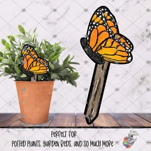 May include: Two orange and black butterfly garden stakes. The stakes are made of wood and have a butterfly design. The butterflies are painted in a realistic style. The stakes are perfect for adding a touch of whimsy to your garden.
