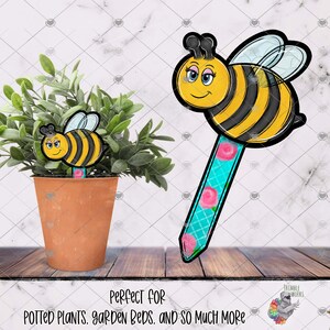 Könnte beinhalten: Eine gelbe und schwarze Biene mit einem blauen und rosa floralen Stock. Die Biene hat ein lächelndes Gesicht und große Augen. Der Text "Perfekt für Topfpflanzen, Gartenbeete und vieles mehr" befindet sich am unteren Rand des Bildes.