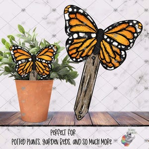 May include: Wooden butterfly garden stakes with orange and black wings. One stake is placed in a terracotta pot with greenery, and another is shown separately. The butterfly stakes are designed for potted plants and garden beds.