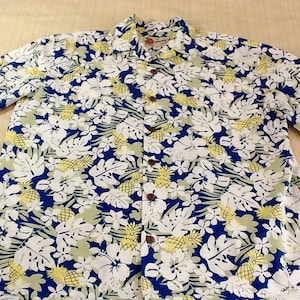 Può includere: Una camicia hawaiana blu, bianca e gialla con stampa di ananas e fiori.