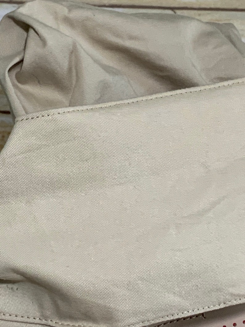 May include: A beige fabric item featuring a prominent rectangular panel with a distinct diagonal twill weave texture. The panel is attached with visible straight stitching along the top edge, while the rest of the material appears soft and folded.