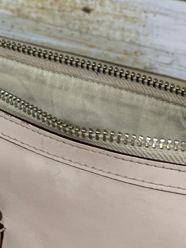 May include: A light beige leather pouch featuring a silver-toned metal zipper closure. The interior is lined with a matching light beige fabric, and the exterior displays clean, precise stitching along the edge of the smooth leather material.