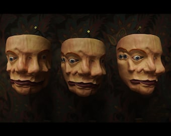 May include: Three beige, sculpted face masks arranged in a row. Each mask features multiple overlapping facial features, including several eyes and noses, with dark red lips. The masks have a textured, skin-like appearance and are mounted on a dark surface.