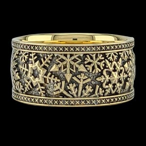 May include: A gold band ring with a black background and a snowflake design. The ring is decorated with a repeating pattern of snowflakes.