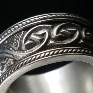 May include: A silver ring featuring a Celtic knot design. The ring is wide and has a textured finish.