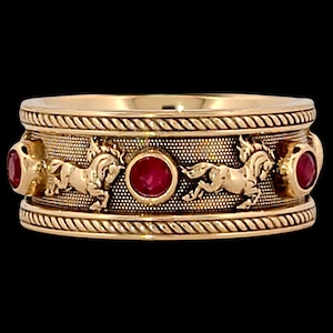 Puede incluir: Un anillo de banda de oro con cuatro piedras preciosas rojas y un diseño de caballos corriendo alrededor de la banda.