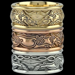 May include: Three stacked rings in gold, copper, and silver tones. Each ring features a detailed relief design of stylized animals and swirling patterns. The rings are displayed against a black background, highlighting their intricate craftsmanship.