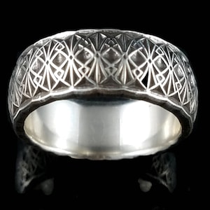 May include: A silver band ring with a geometric design. The ring is engraved with a repeating pattern of triangles and lines.