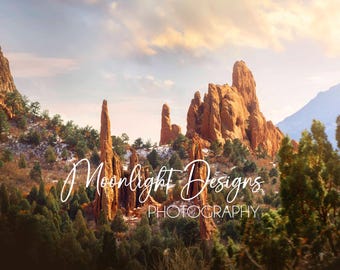 May include: A scenic landscape photograph of red rock formations in a mountainous area. The sky is a soft blue with white clouds. The rocks are tall and thin, with some appearing to be spires. The foreground is covered in green trees and bushes. The text "Moonlight Designs Photography" is superimposed on the image.