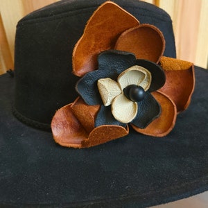 May include: A black felt hat with a brown and black leather flower embellishment.