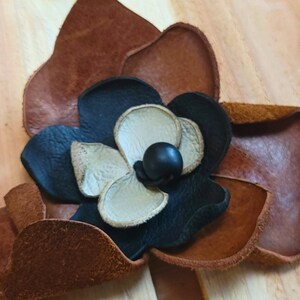 May include: A brown leather flower with a black and white center. The flower is made of different pieces of leather sewn together.